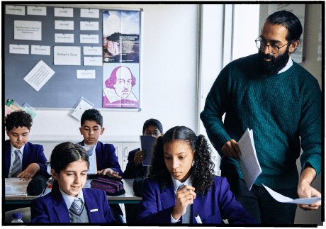 A teacher handing out worksheets to pupils in a classroom
